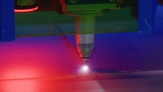 Průmyslový laserový gravírovací stroj řezací kovovou desku, vyzařující červená a modrá světla, ve výrobním procesu vykazující přesnost a technologii