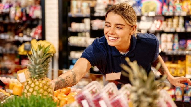 Prodavačka v supermarketu upravuje ananas a další zboží v regálu