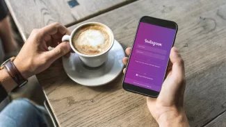 Muž s kávou drží telefon s přihlašovací stránkou Instagramu.