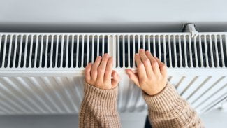 Dětské ruce v hnědém svetru si ohřívají ruce na topení.