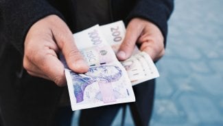 Muž drží v ruce bankovky v hodnotě 1000 Kč a 200 Kč.