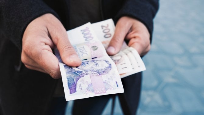 Muž drží v ruce bankovky v hodnotě 1000 Kč a 200 Kč.