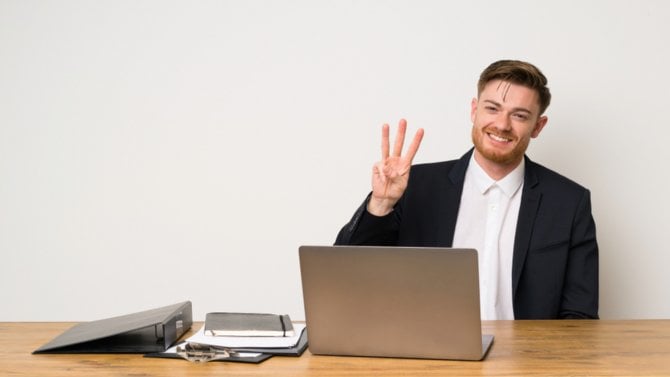 Muž v kanceláři u počítače počítá na prstech do tří