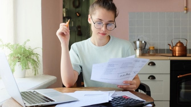 Žena u počítače si prohlíží papír a provádí výpočty