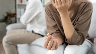Žena drží v ruce snubní prstýnek, druhou rukou se chytá za hlavu po hádce s manželem.