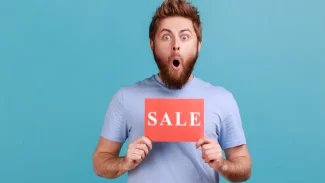 Mladý muž s udiveným výrazem s vykulenýma očima s cedulí v rukách s nápisem sale