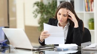 Žena sedící za kancelářským stolem studuje zamyšleně papírový dokument