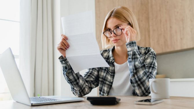 Mladá žena v brýlích pečlivě studuje papírový dokument