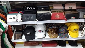 Na obrázku je vyobrazeno zboží na poličkách ve vietnamské tržnici. Jedná se o padělky peněženek a kšiltovek známých značek.