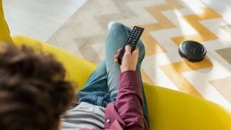 selektivní zaostření na muže, který sedí na pohovce a sleduje film, zatímco robotický vysavač vysává koberec v obývacím pokoji