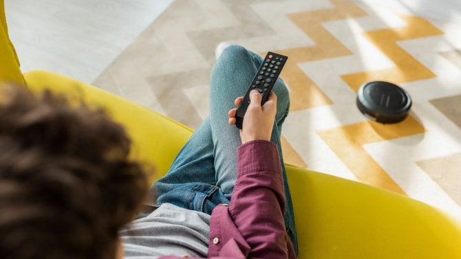 selektivní zaostření na muže, který sedí na pohovce a sleduje film, zatímco robotický vysavač vysává koberec v obývacím pokoji
