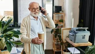 Senior v pracovním procesu, telefonuje a usmívá se. V ruce drží kávu