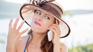 Žena v klobouku a v plavkách drží u ucha telefon a tváří se naštvaně