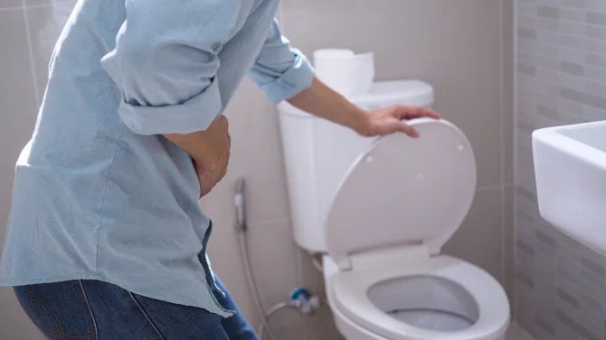Muž s bolestmi břicha zvedající poklop záchoda