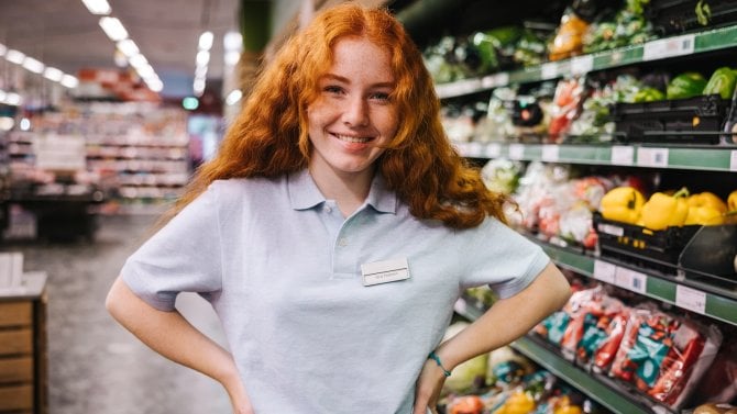 https://i.iinfo.cz/images/Mladá brigádnice se zrzavými vlasty stojí v supermarketu v oddělení ovoce a zeleniny.