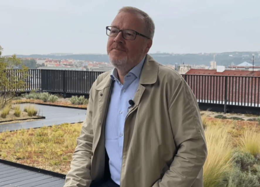 Muž v béžové bundě sedící na terase.