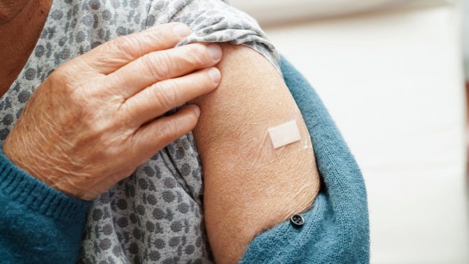 Detail levé paže seniorky s náplastí po očkování