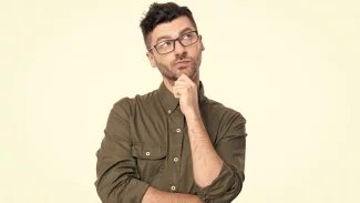 Mladý muž v brýlích stojí a tváří se zamyšleně. Jednou rukou si podpírá bradu