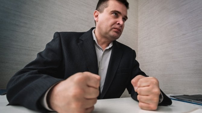 Muž, který sedí u stolu a má zatnuté pěsti