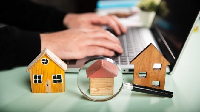 Makety domů s lupou a počítačem v pozadí