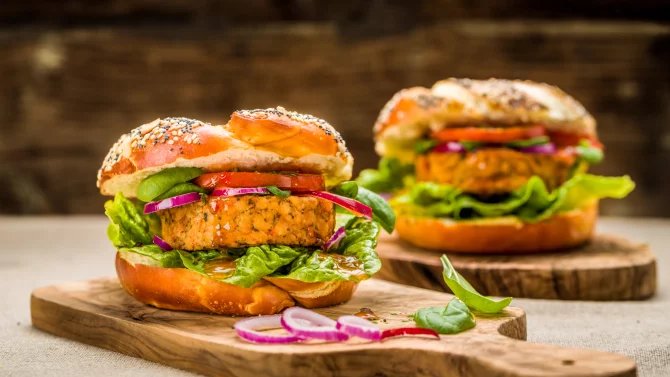 Dva vegetariánské hamburgery na dřevěném prkénku.