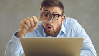 Muž u počítače má lupu a něco sleduje na počítači