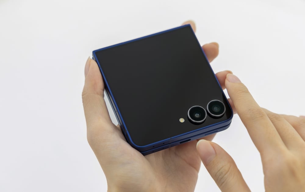 Složený tmavě modrý Samsung Galaxy Z Flip7 v rukou, s dvojicí fotoaparátů a USB-C konektorem.