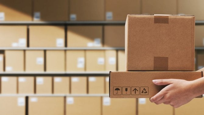 Skladník držící dodací krabice a naskládané balíky v pozadí, koncept logistiky a přepravy