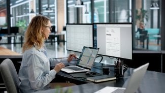 Žena se v kanceláři na několika monitorech zorientovává v práci