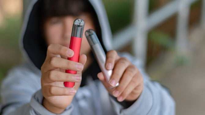 Dospívající kluk drží v ruce dvě e-cigarety