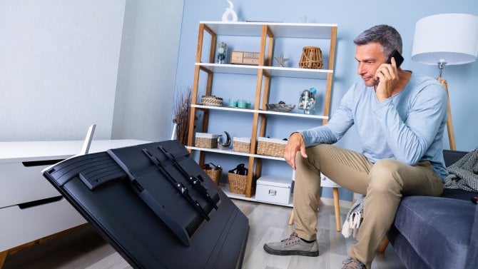 Muž sedící před televizí, která spadla na zem.