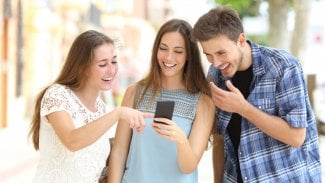 Mladí lidé se smějí něčemu na mobilním telefonu