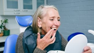 Starší žena si v zubařském křesle prohlíží zuby
