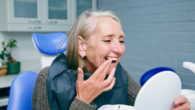 Starší žena si v zubařském křesle prohlíží zuby