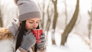 Mladá žena zabalená do šály a čepice pije horký nápoj