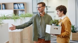 Zaměstnanec s osobními věcmi a s kytkou v krabici vstupuje do kanceláře