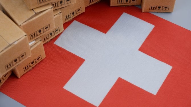 Koncept výrobků vyrobených ve Švýcarsku. Švýcarská vlajka a detailní záběr na mnoho kartonových krabic.