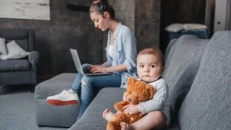 Matka pracující na počítači a vedle ní sedí malé dítě.