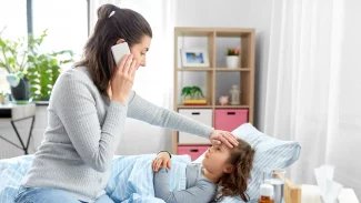 Matka s telefonem u ucha sahá na čelo nemocnému dítěti