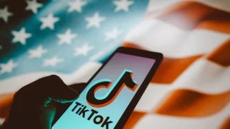 Mobil se zapnutou aplikací TikTok, na pozadí vlajka Spojených států amerických