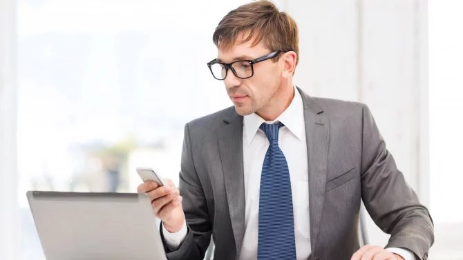 Muž v kanceláři hledá informace v mobilu