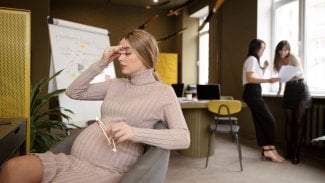 Těhotná žena sedí v práci na židli a odpočívá