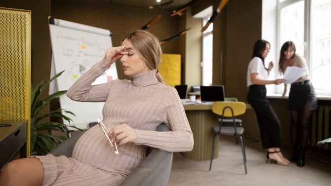 Těhotná žena sedí v práci na židli a odpočívá