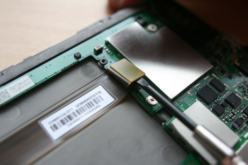 Teď odpojíme displej. Je to ten dlouhý plochý vodič, který byl pod baterií. Stačí jej podebrat šroubováčkem a opět směrem vzhůru vytáhnout z konektoru.