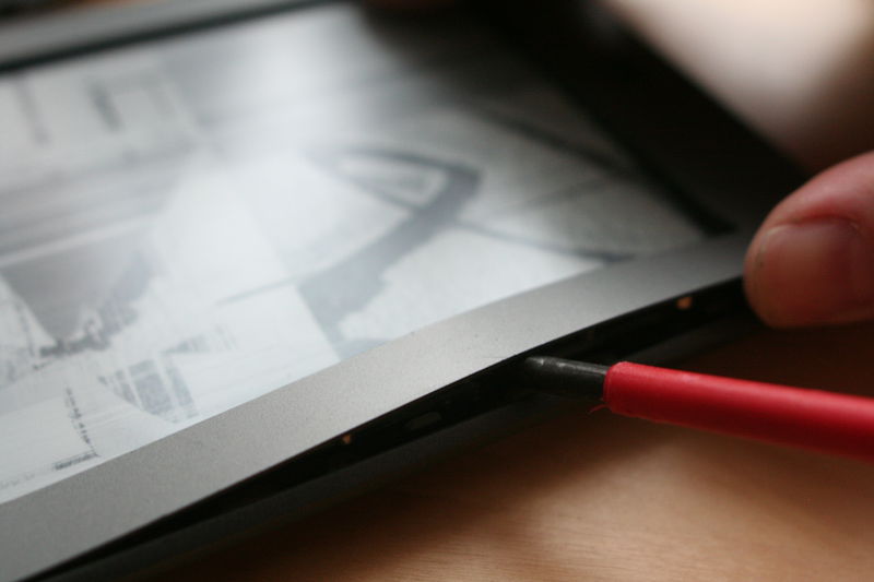 Poté čtečku otočíme a sundáme přední kryt. Držely ho šroubky, které jsme před chvíli odšroubovali, ale kryt je navíc ještě přilepený. Nebojte se proto zabrat. Pod plastovým krytem je ještě tenký plech, ten budete odlepovat s ním. Nebojte.