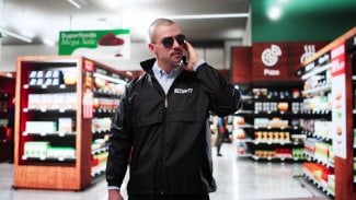 Pracovník ostrahy v černé uniformě a černých brýlích stojí uprostřed obchodu.