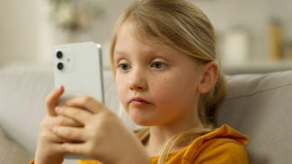 Blonďatá dívka má v ruce mobilní telefon.