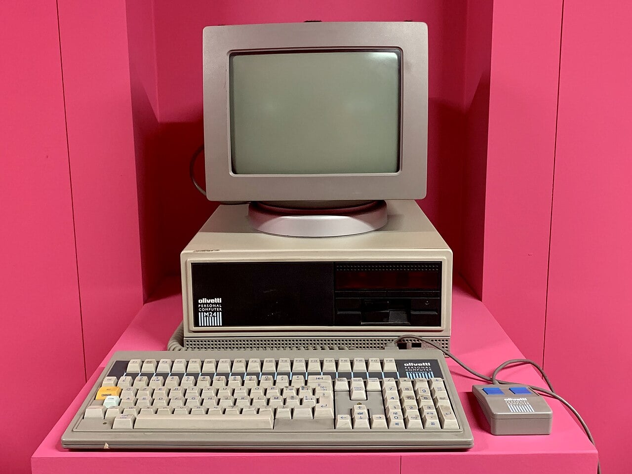 Béžový počítač Olivetti M24 s monitorem a klávesnicí v muzejní expozici.