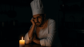 Naštvaný kuchař, který sedí u svíčky v kuchyni bez elektrického proudu.