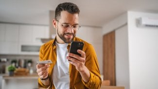 Mladý muž nakupuje na mobilu a platí kartou